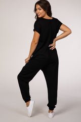 woman wearing a black short sleeve jumpsuit, styled for maternity wear, with a relaxed fit and back button detail