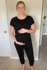 woman wearing a black short sleeve maternity jumpsuit and holding her baby bump
