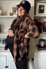 woman wearing a black maternity dress and an orange and black plaid shirt, showing her baby bump and smiling