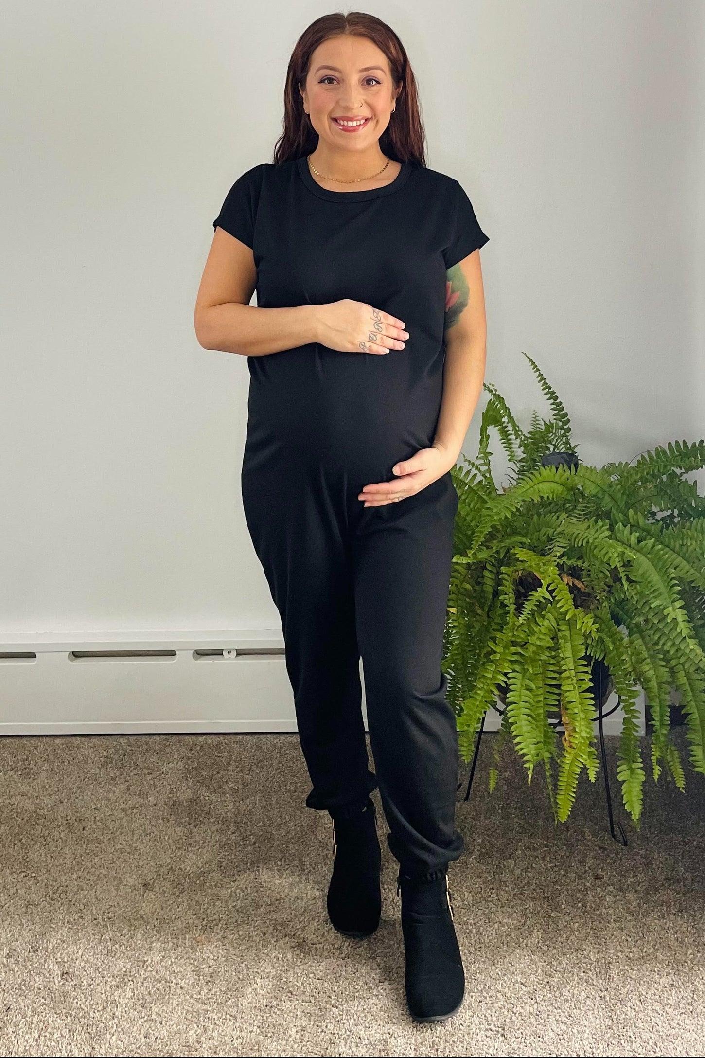woman wearing a black maternity jumpsuit and holding her baby bump