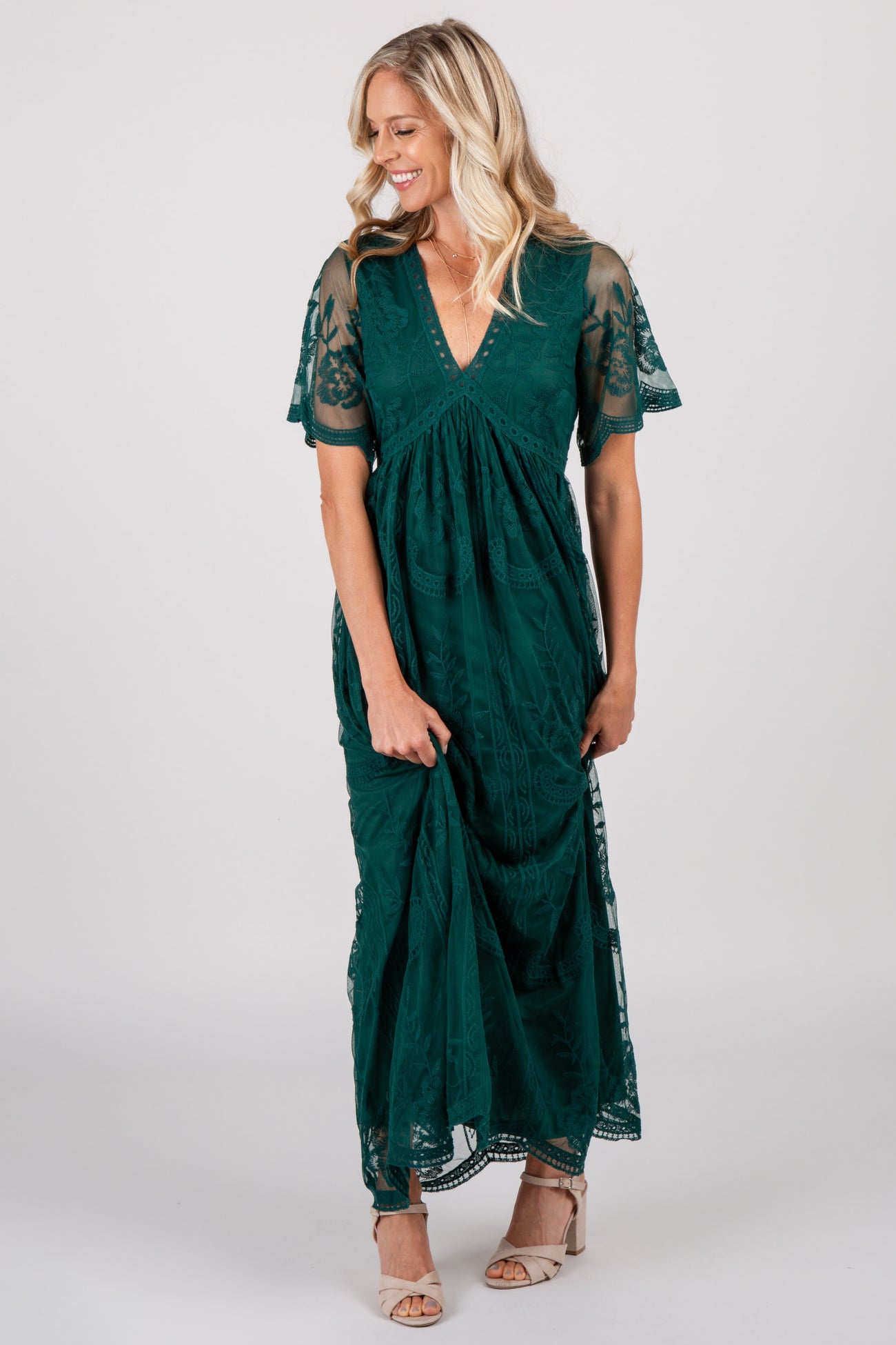 woman wearing a dark green lace maxi dress with short flutter sleeves and beige heels