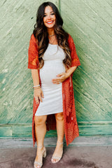 woman wearing a gray maternity dress with a red lace kimono and holding her baby bump