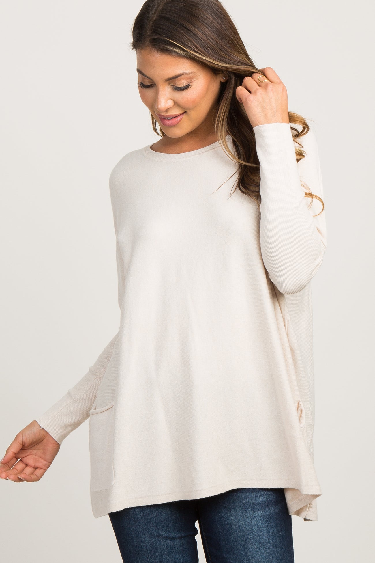 smiling pregnant woman wearing a cream long sleeve maternity tunic sweater and dark jeans