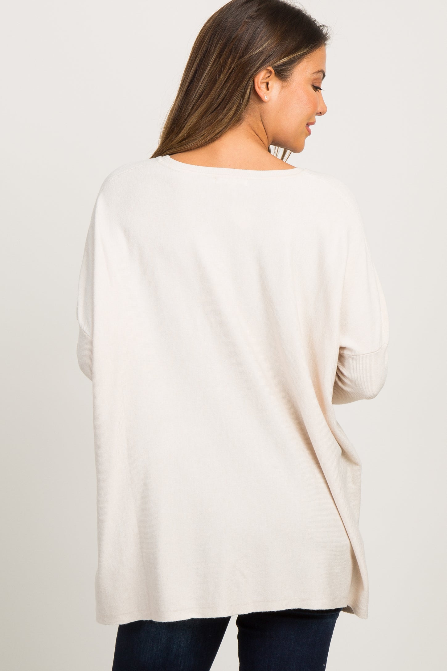 Back view of a woman wearing an oversized cream knit sweater with drop shoulders and ribbed cuffs