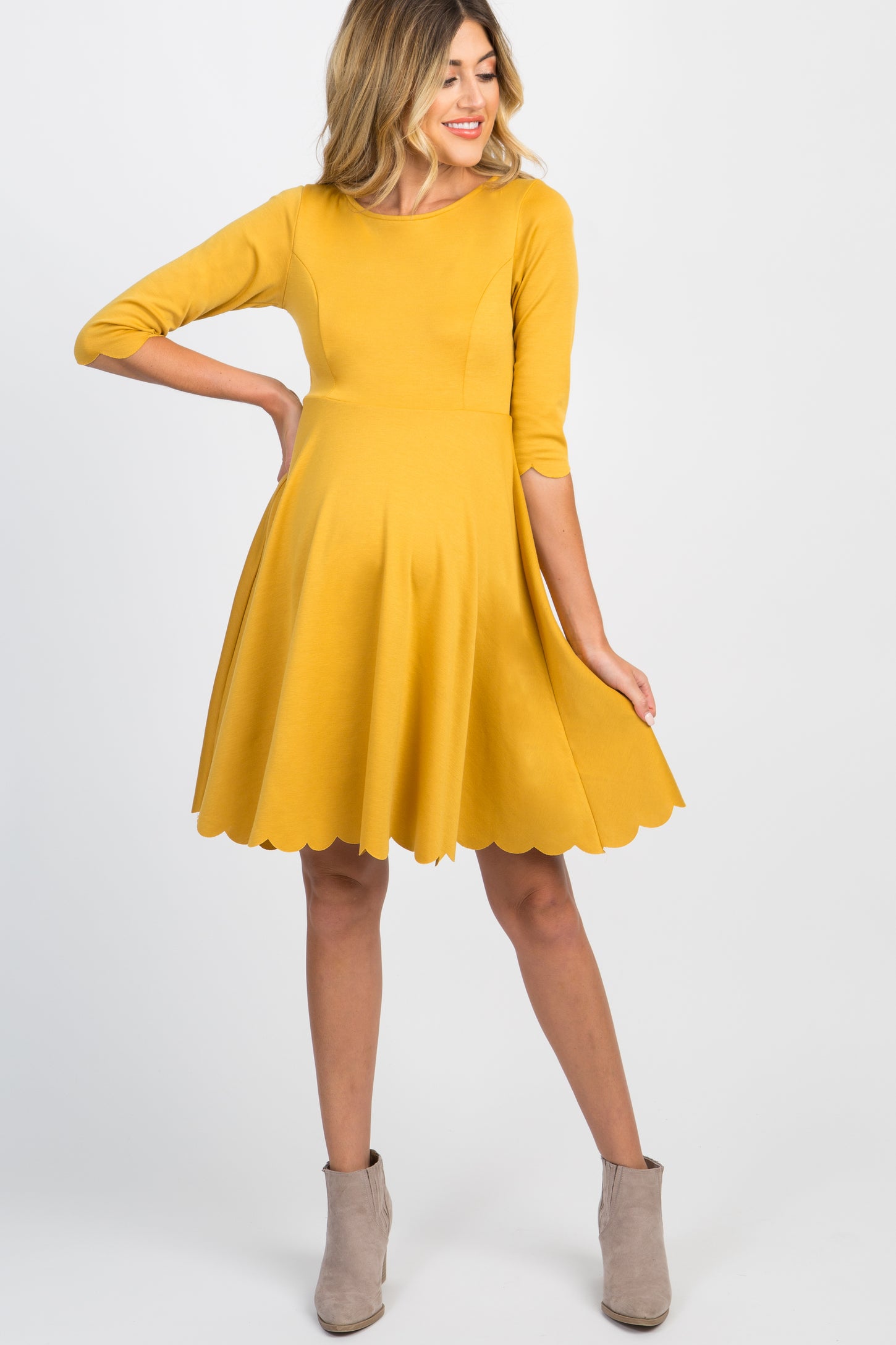 pregnant woman wearing a mustard yellow maternity dress with scalloped hem and grey ankle boots