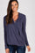 smiling woman wearing a navy blue long sleeve draped wrap top and dark wash jeans