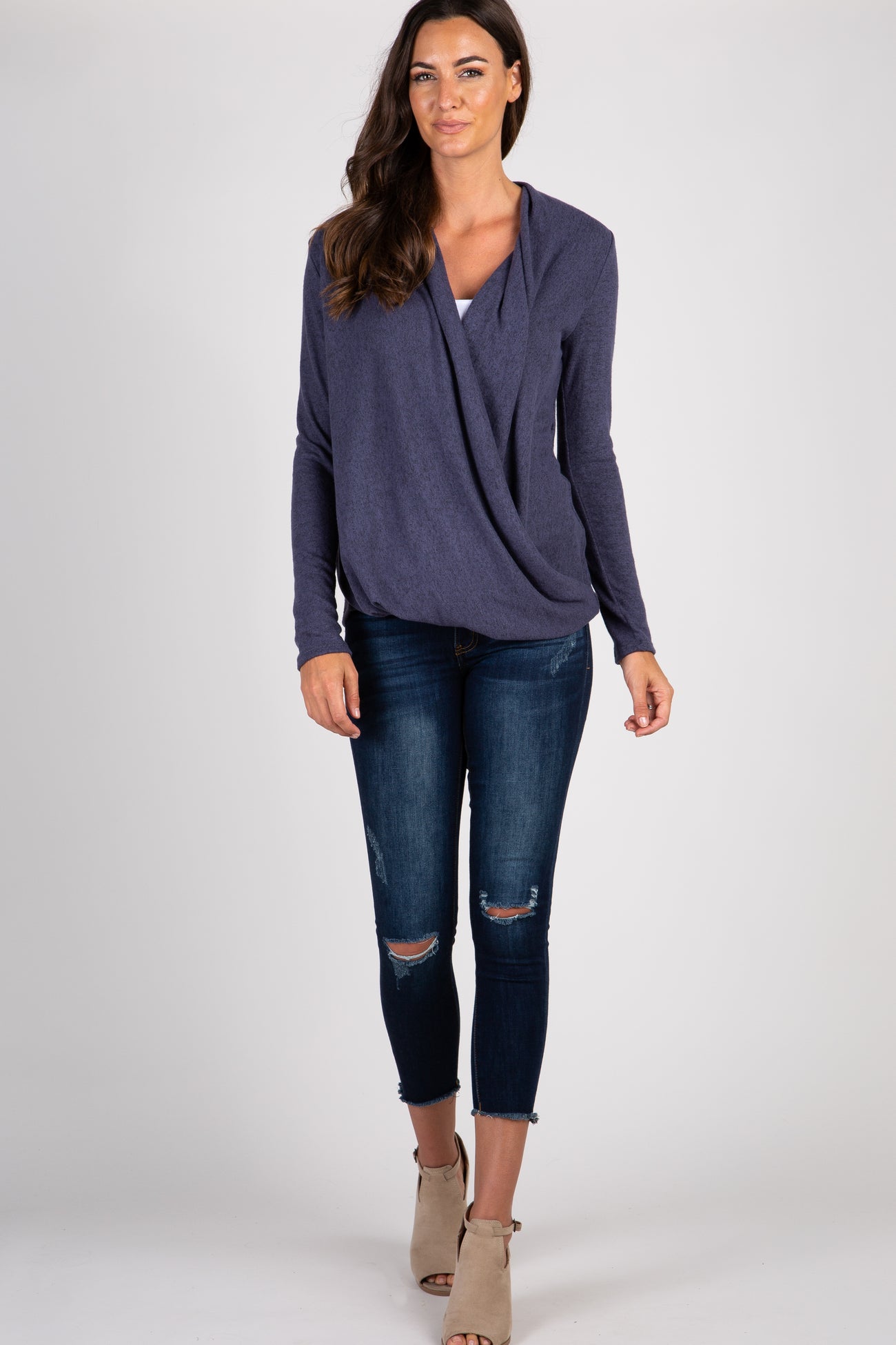 woman wearing a purple long sleeve draped front top and distressed blue skinny jeans