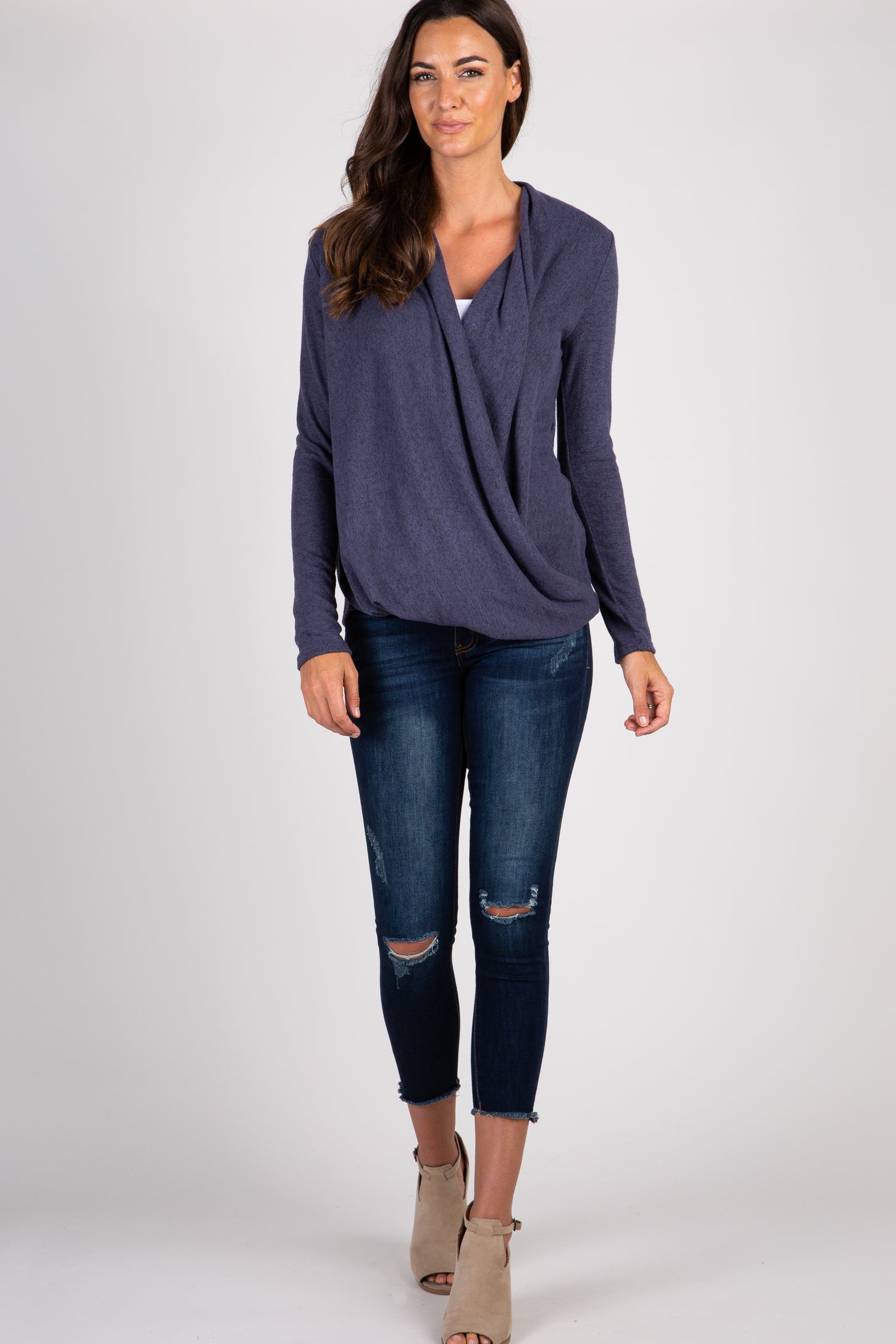 woman wearing a purple long sleeve draped front top and distressed blue skinny jeans