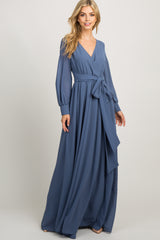 woman wearing a long sleeve blue maternity maxi dress with a wrap front and waist tie