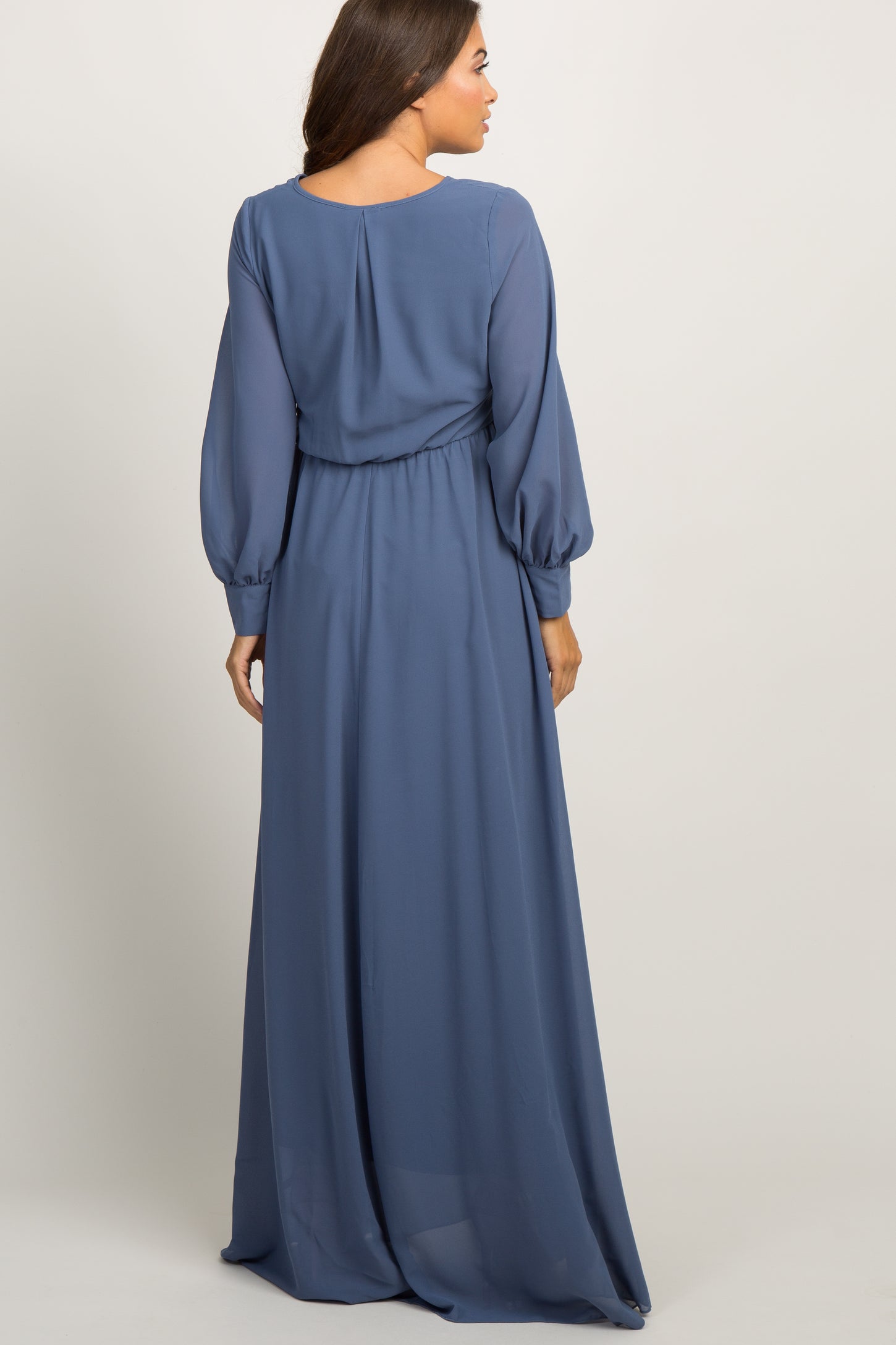Woman wearing a long sleeve slate blue chiffon maxi dress with a pleated waist and button cuffs