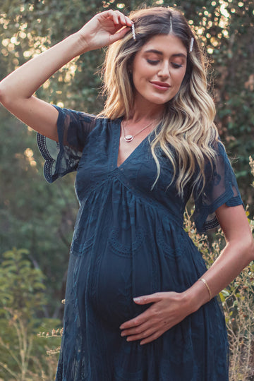 woman wearing a navy blue lace maternity dress, cradling her baby bump in an outdoor setting