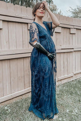 woman wearing a navy blue maternity dress with sheer sleeves, posing with her baby bump visible against a wooden fence