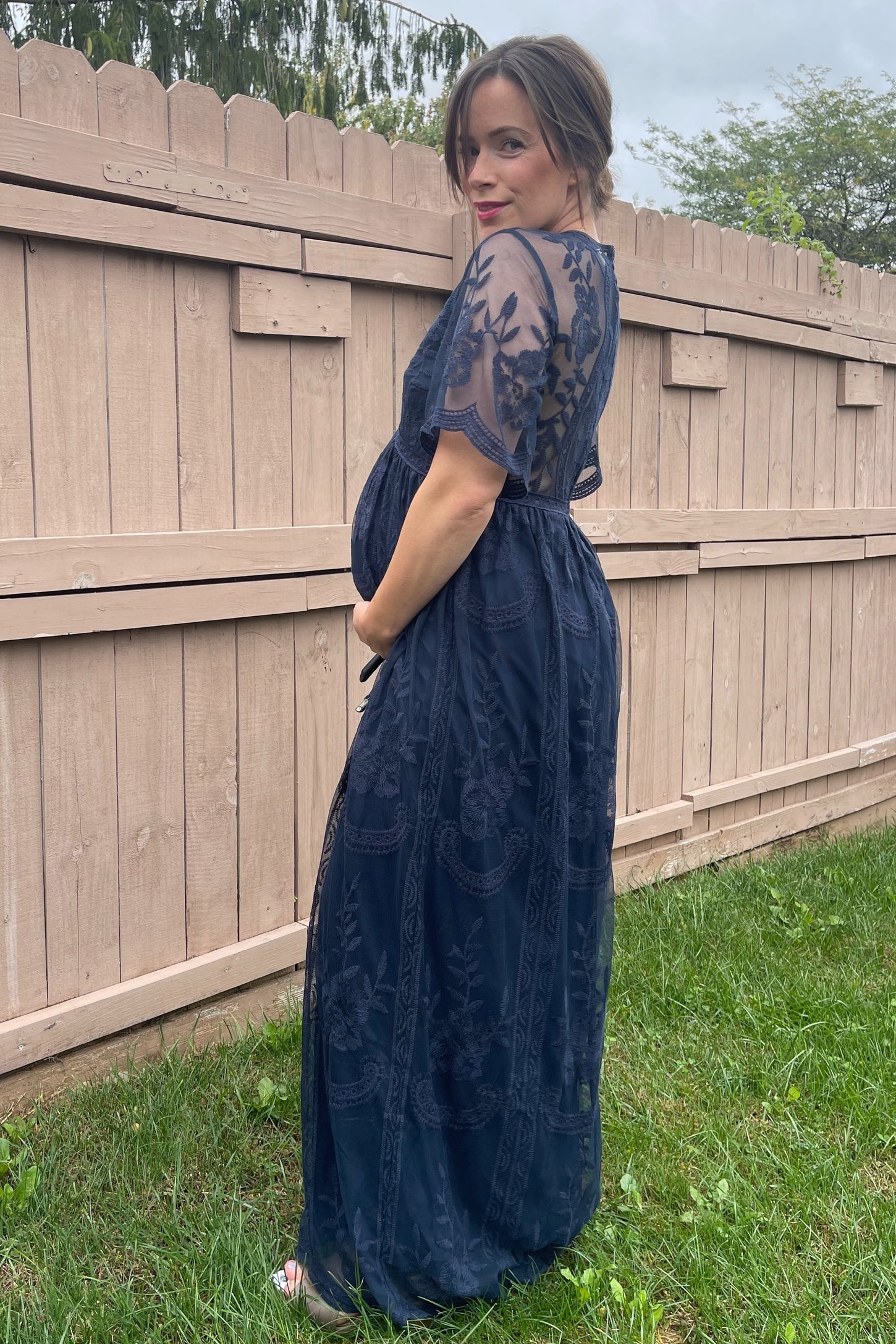woman wearing a navy blue maternity gown with lace detailing and a visible baby bump