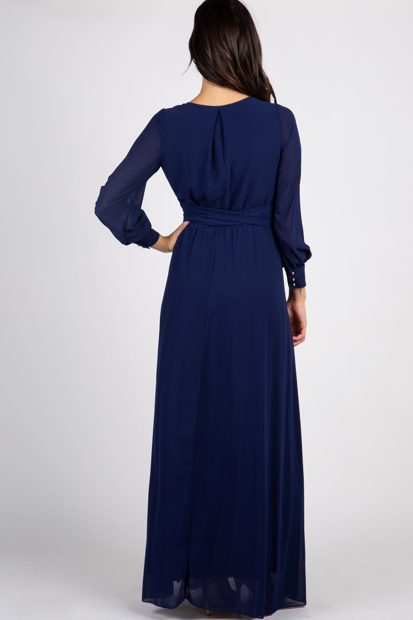 Back view of a woman wearing a long navy blue chiffon maxi dress with long sleeves and a cinched waist
