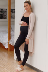 woman wearing a black maternity tank top and high-waisted black leggings, styled with a light pink cardigan and showing her baby bump