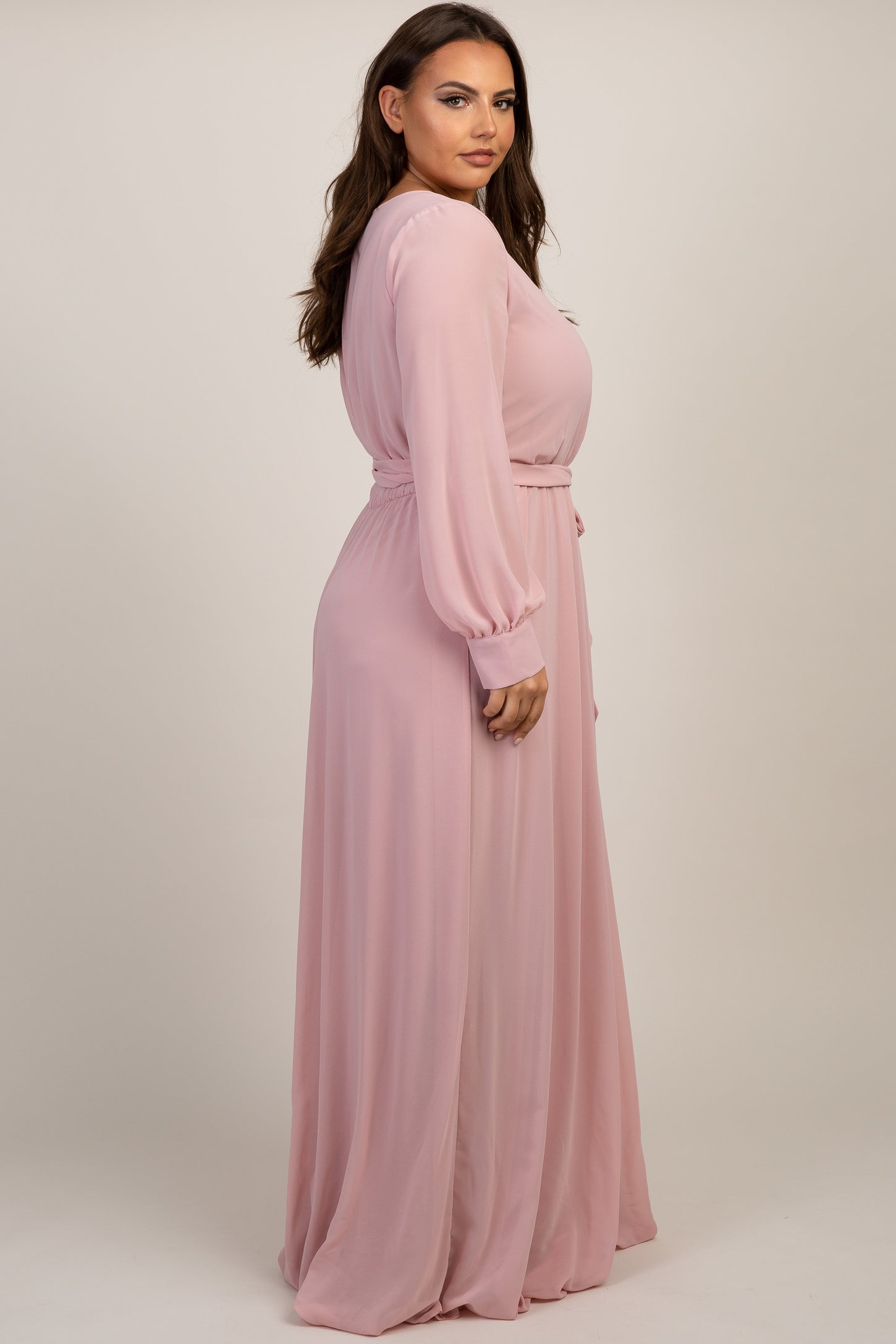 woman wearing a long sleeve light pink chiffon maxi dress with a belted waist