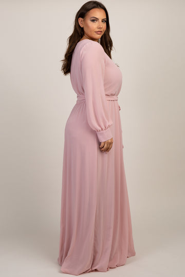 woman wearing a long sleeve light pink chiffon maxi dress with a belted waist