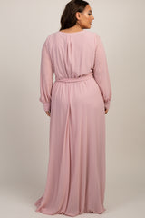 Back view of a woman wearing a long sleeve light pink maxi dress with a belted waist