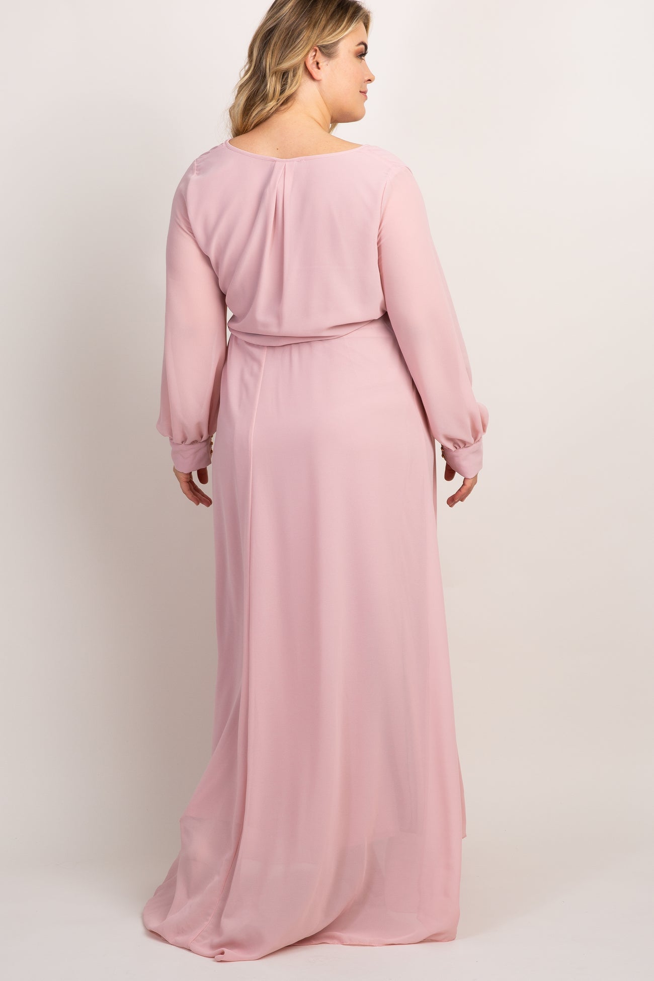 Back view of a woman wearing a long sleeve light pink maxi dress with a belted waist