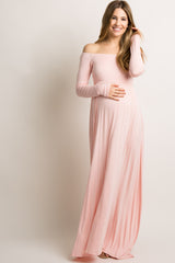 woman wearing a light pink off-the-shoulder maternity maxi dress and holding her baby bump
