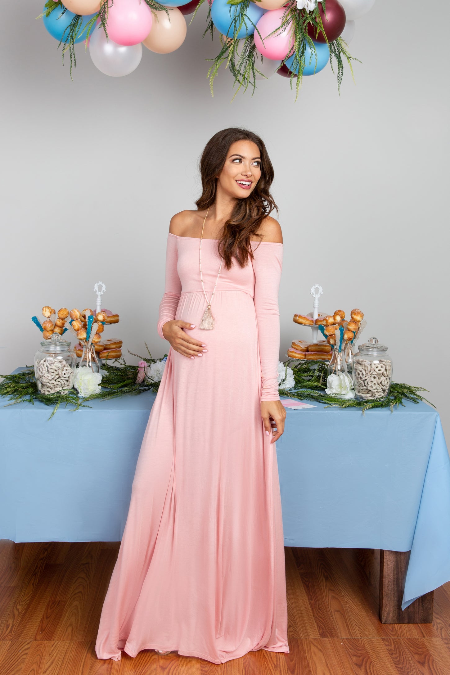 woman wearing a pink off-shoulder maternity dress and holding her baby bump at a celebration table