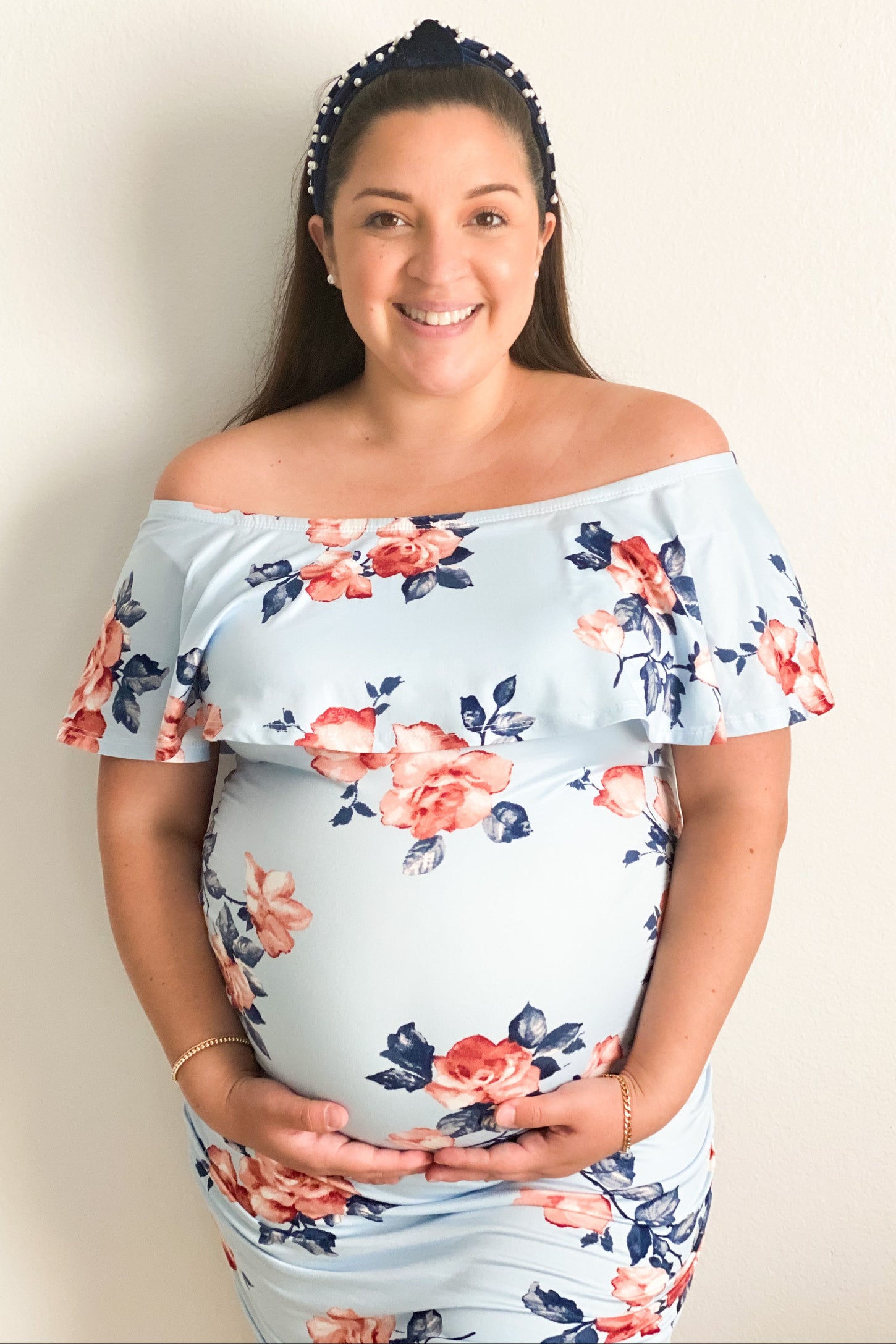 woman wearing a light blue off-the-shoulder maternity dress with floral print and holding her baby bump