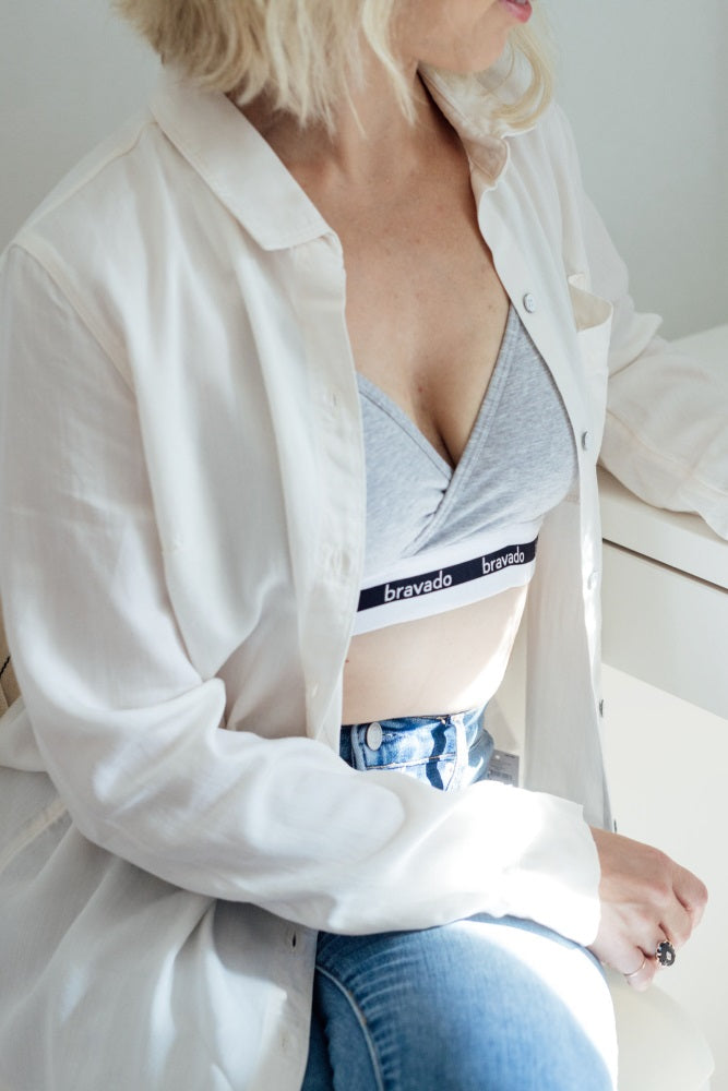 woman wearing a grey Bravado nursing bra under an open white button-down shirt and blue jeans