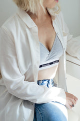 woman wearing a grey Bravado nursing bra under an open white button-down shirt and blue jeans
