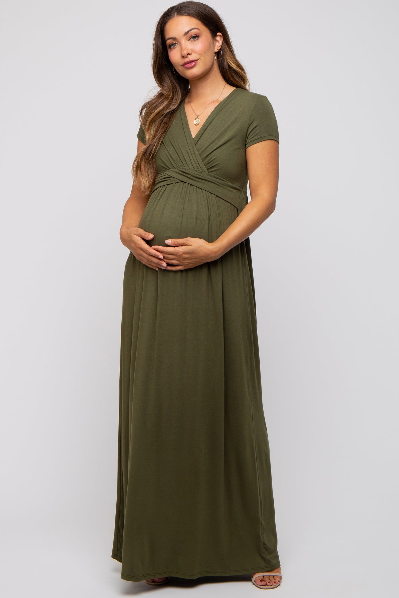 woman wearing a dark olive green maternity maxi dress with short sleeves and a wrap bodice holding her baby bump