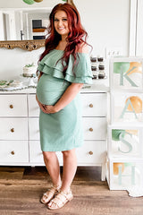 woman wearing a mint green off-shoulder maternity dress with ruffles and holding her baby bump