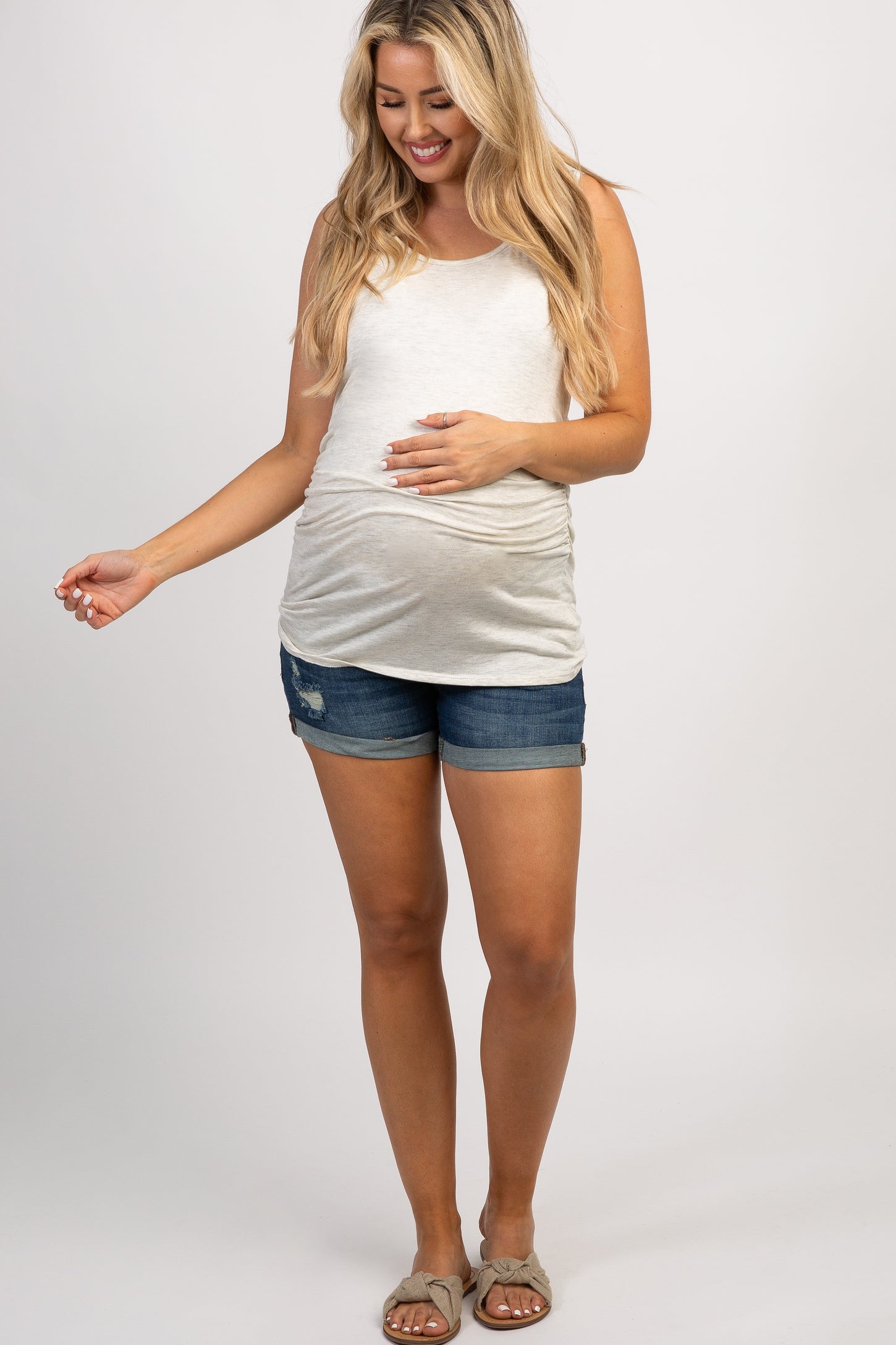 woman wearing a teal short sleeve maternity top and denim shorts, showing her baby bump