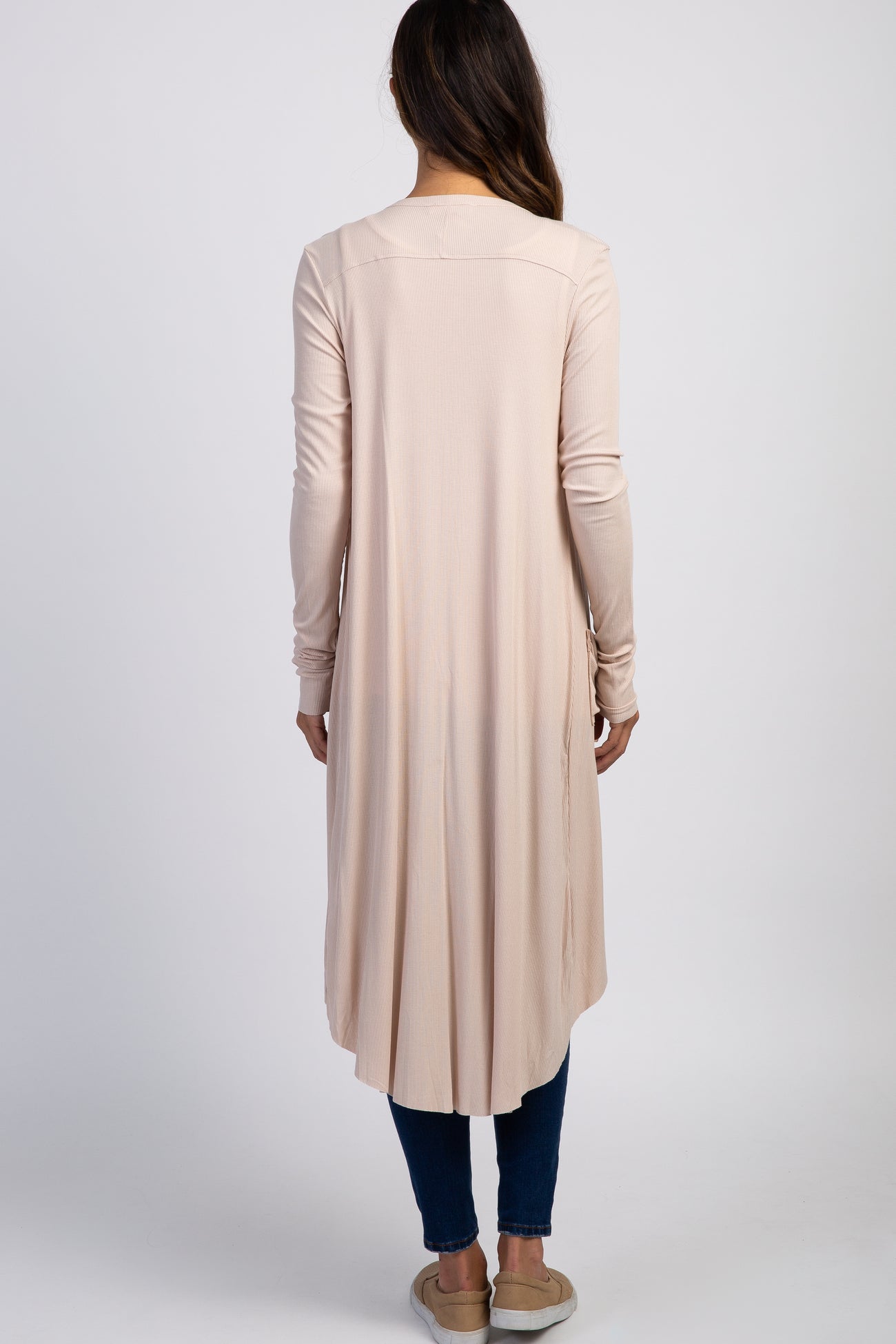 back view of woman wearing long light pink ribbed cardigan with high-low hem and blue jeans