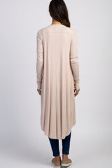 back view of woman wearing long light pink ribbed cardigan with high-low hem and blue jeans
