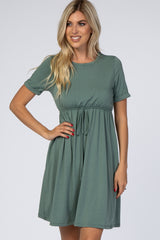 woman wearing a short sleeve green drawstring waist dress with a flared skirt, smiling at the camera