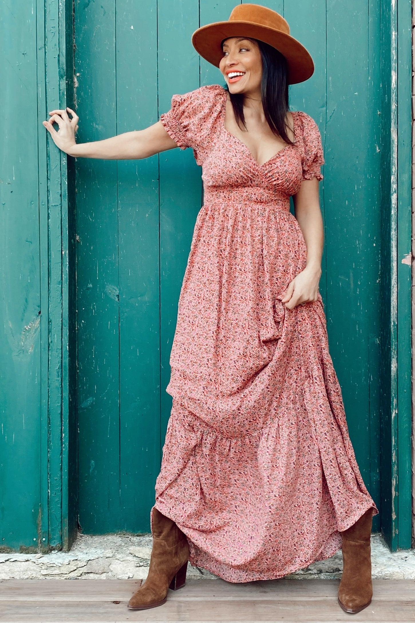 woman wearing a pink floral maxi dress with puff sleeves and a deep v-neck, accessorized with a brown wide-brimmed hat and tan boots