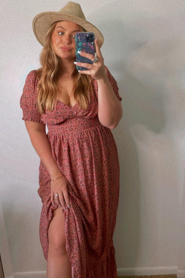 woman wearing a floral print maxi dress with puff sleeves and a thigh-high slit, accessorized with a wide-brimmed hat