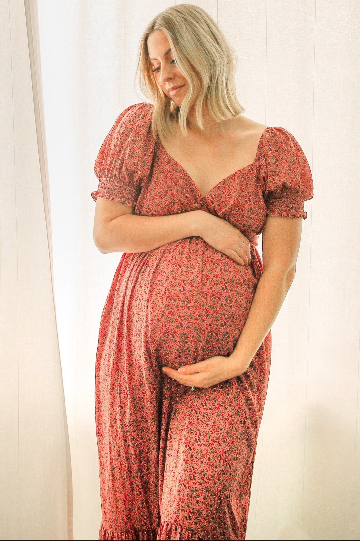 woman wearing a red floral maternity dress with puff sleeves and holding her baby bump