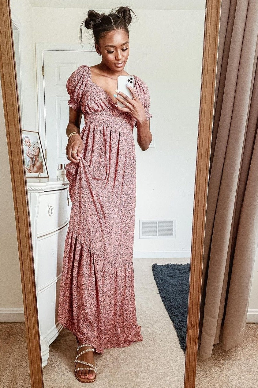 woman wearing a pink floral maxi dress with puff sleeves and a tiered skirt, standing in front of a mirror