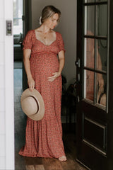 woman wearing a red floral maternity dress with puff sleeves, holding a straw hat and cradling her baby bump