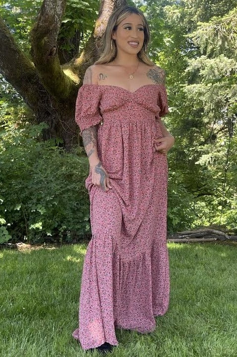 woman wearing a pink floral maxi dress with off-the-shoulder sleeves standing in a green outdoor setting