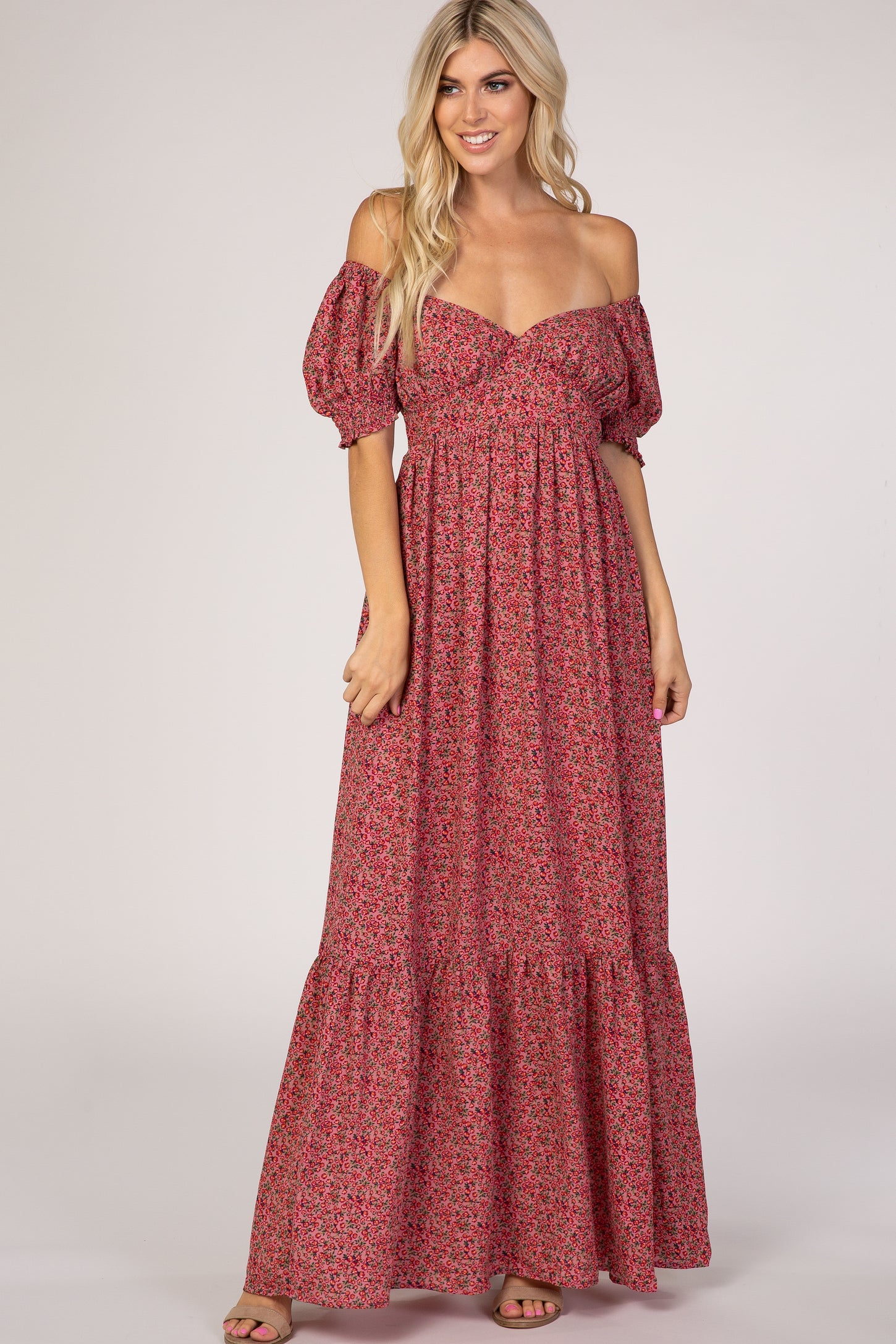 woman wearing a pink floral off-the-shoulder maxi dress with puff sleeves and a tiered skirt