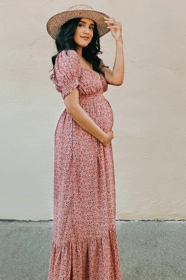 woman wearing a pink floral maternity maxi dress with puff sleeves and holding her baby bump