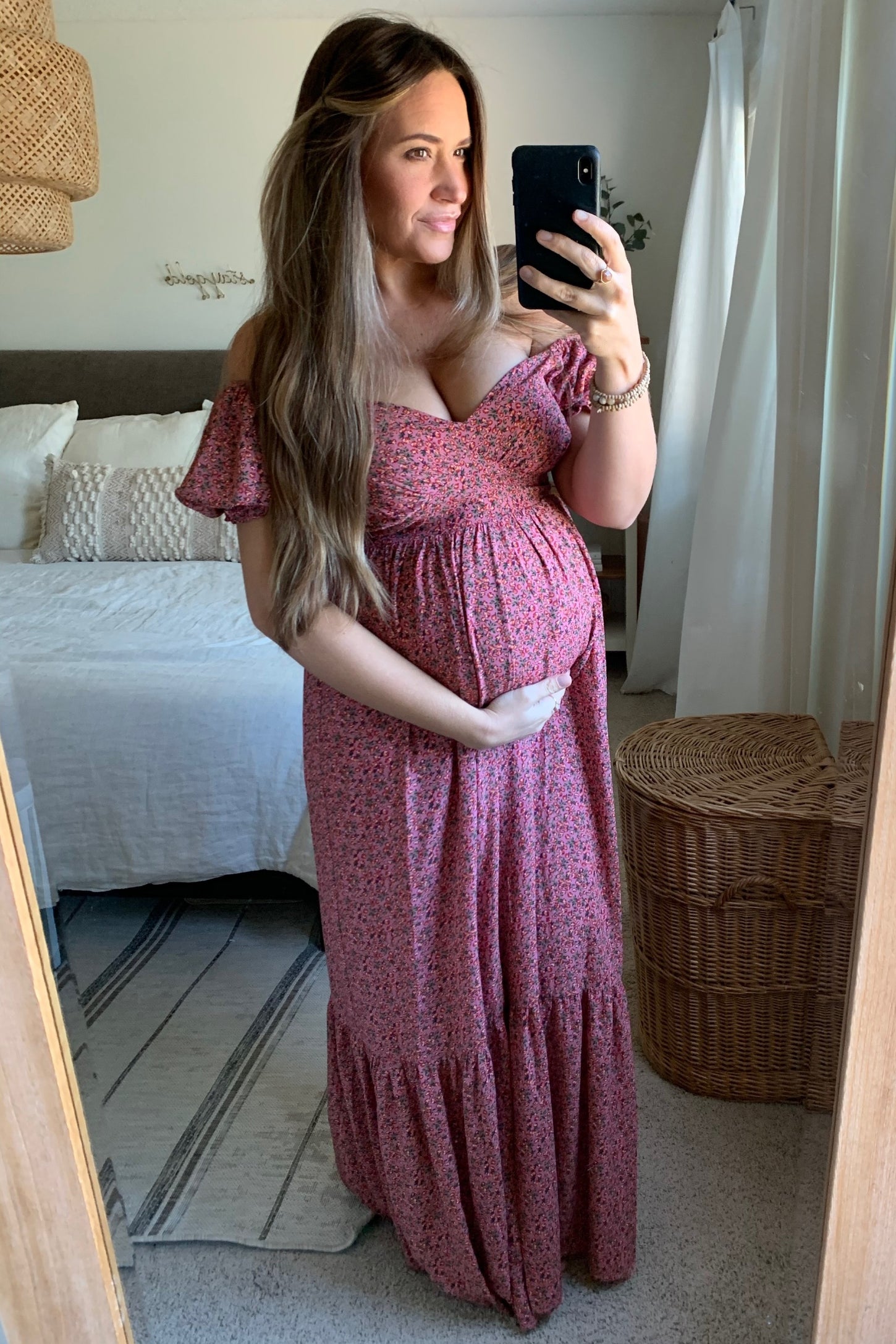 woman wearing a pink floral off-the-shoulder maternity dress and holding her baby bump