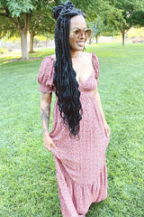 woman with long black braids wearing a pink floral maxi dress and oversized sunglasses in a park