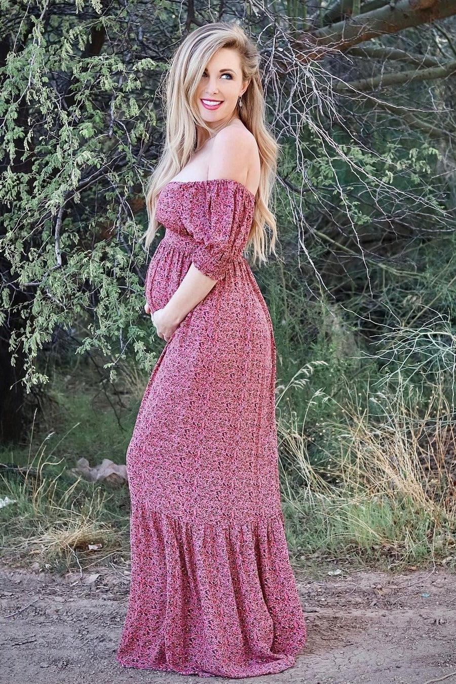 woman wearing a pink floral off-the-shoulder maternity maxi dress and holding her baby bump