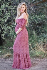 woman wearing a pink floral off-the-shoulder maternity maxi dress and holding her baby bump
