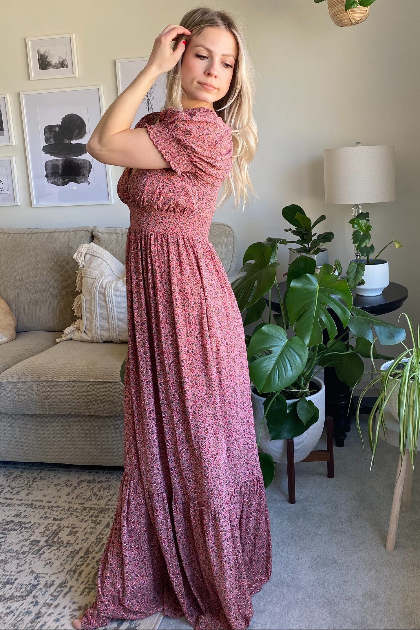 woman wearing a pink floral maxi dress with short sleeves and a tiered skirt, posing in a bright living room