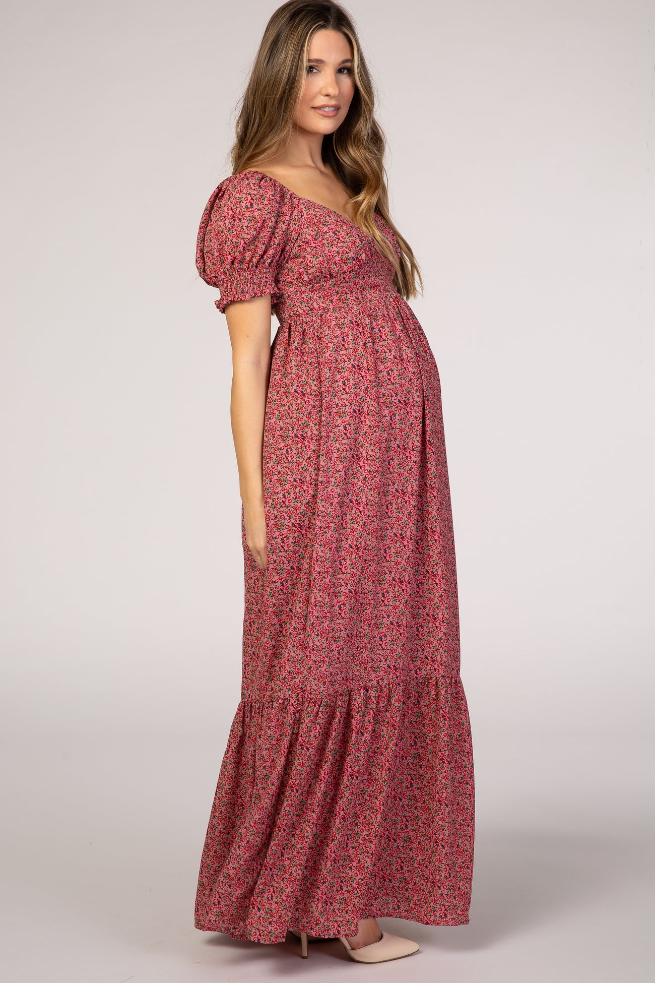 woman wearing a pink floral maternity maxi dress with puff sleeves and a gathered skirt, showcasing her baby bump