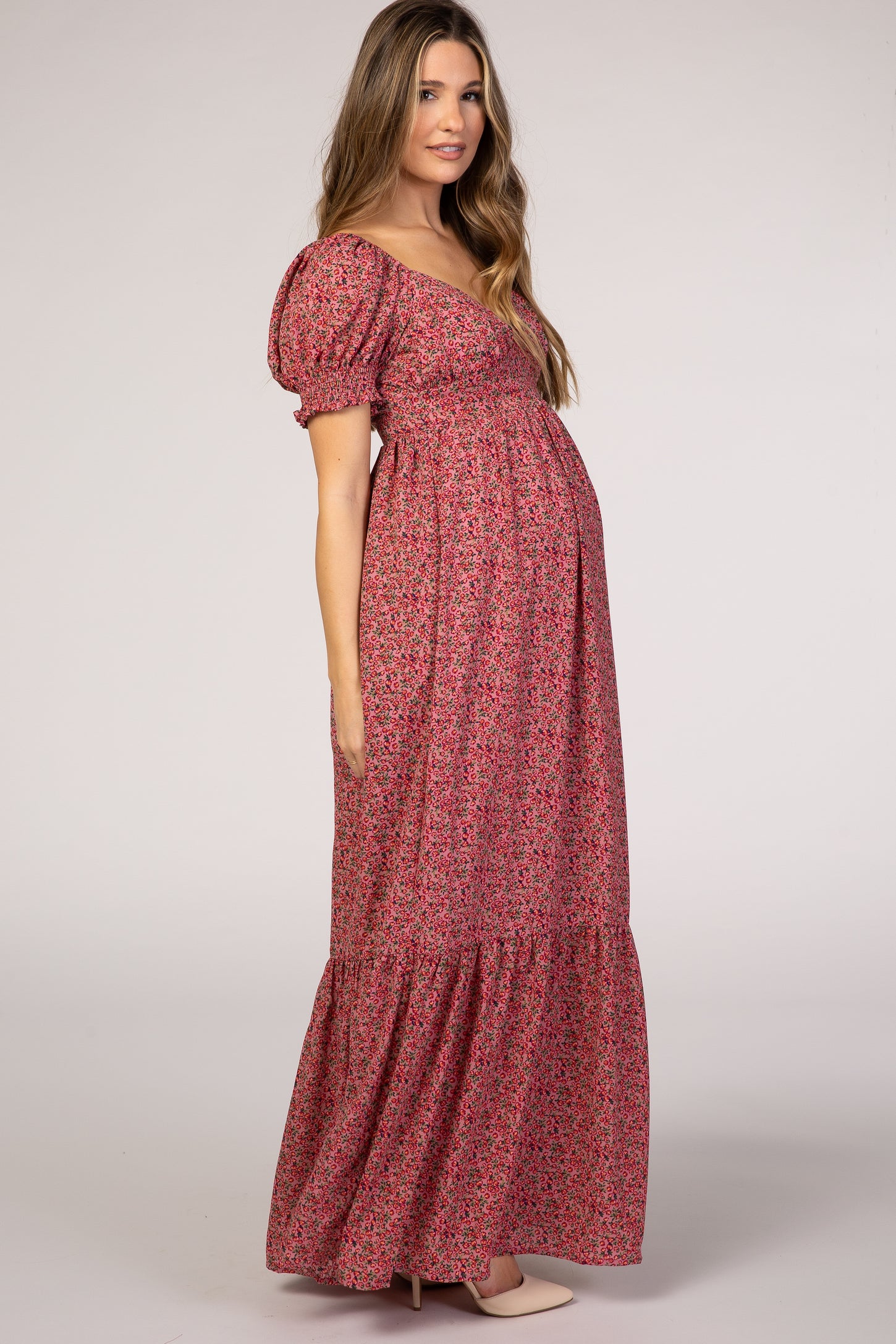 woman wearing a pink floral maternity maxi dress with puff sleeves and a gathered skirt, showcasing her baby bump