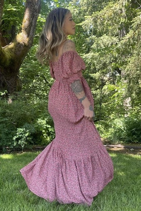 woman in pink floral off-the-shoulder maxi dress standing in a lush green garden setting